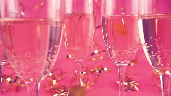 Falling confetti on glasses with sparkling wine on a pink background with serpentine. Slow motion.