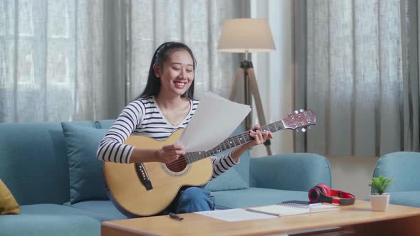 Asian Woman Composer Holding And Looking At Paper Then Playing A Guitar At Home