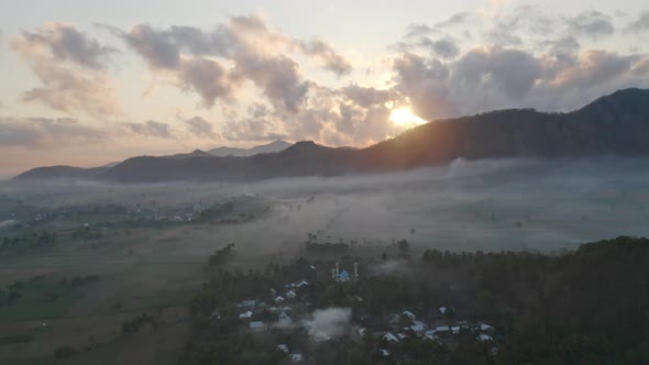 View From Above of Plain Fields Surrounded By White Mist and Sun Rising Behind Forest Mountain