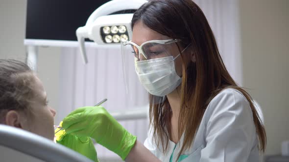 Friendly Female Dentist Examines Teeth of a Cute Little Girl Using Her Instruments