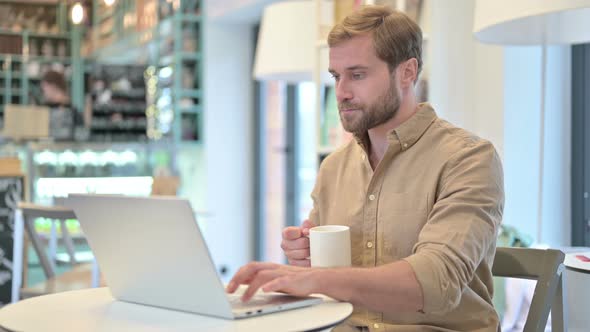 Attractive Man Drinking Coffee Working on Laptop 