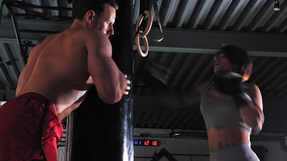 Woman Boxer Training Her Punches on Punching Bag with Her Trainer Holding It