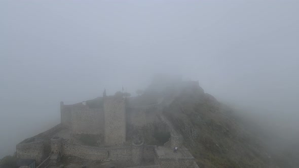 A drone rises above castle Marvão through the thick mist.