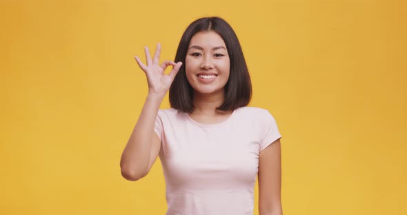 Cute Young Asian Woman Gesturing Ok Sign and Smiling, Orange Studio Background