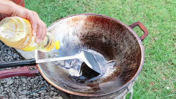 Chef´s hand pouring vegetable oil into hot frying pan to prepare to cook outdoor