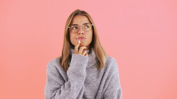 Young Woman is Touching Her Chin Thinking About Something While Posing Against Pink Studio
