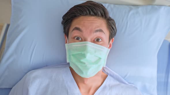 Asian young male patient wearing protective facemask lying on bed, waiting for treatment from docto.