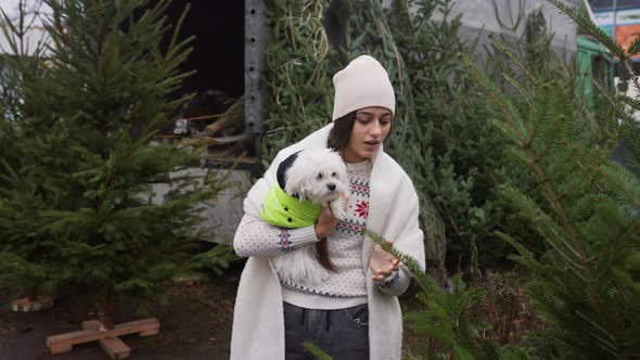 Woman with a White Dog in Her Arms Near a Green Christmas Trees