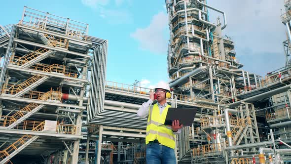 Engineer is Standing Next to the Oil Refinery and Talking Over Radio