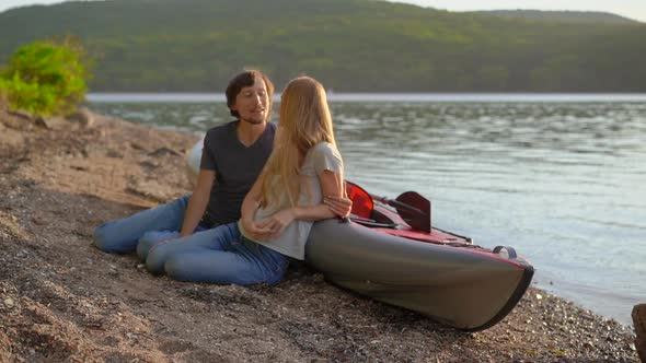 Young Man and Woman Sit By Their Inflatable Kayak on a Lake or Seashore. Slowmotion Shot