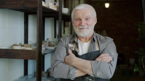 Portrait of Cheerful Senior Ceramist Standing in Workshop Wearing Apron and Smiling