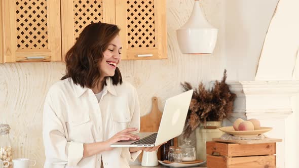 a Young Attractive Woman in a Bright Modern Kitchen Uses a Laptop for Video Communication