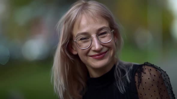 Close-up Portrait of a Young Smiling Blonde Woman with Glasses Posing Walking Around the City on an