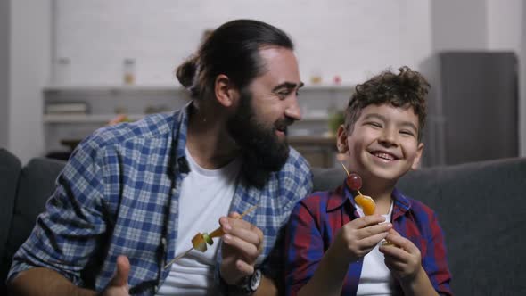 Carefree Smiling Dad and Son Enjoying Tv Show