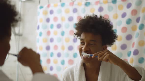 Afro Man Brushing Teeth with Toothbrush Standing Near Mirror in Bathroom