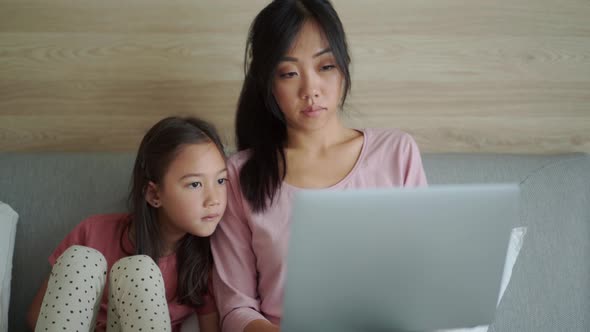 Cute Asian mom and daughter looking at laptop