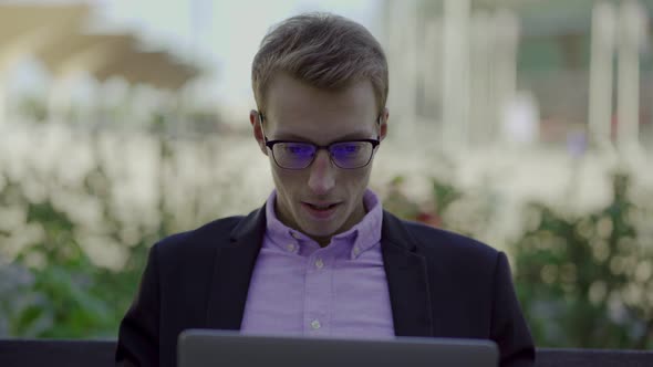 Cheering Young Man Sitting in Park with Laptop