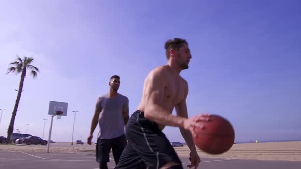 A man takes a layup shot while playing one-on-one basketball hoops on a beach court.