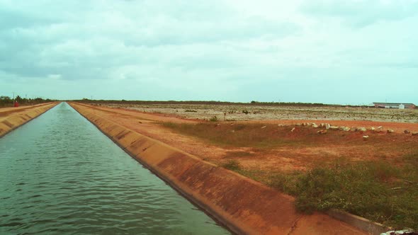 Still view of a manmade waterway in a rural area with a barren field in the background