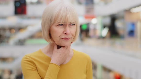 Mature Middle Aged Caucasian Woman Standing in Public Place Holding Neck Suffering From Sore Throat