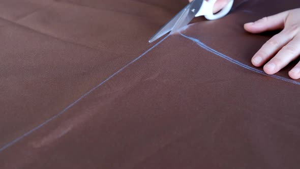 Woman Hands with Scissors Cutting Brown Fabric According to Markings on Tabletop