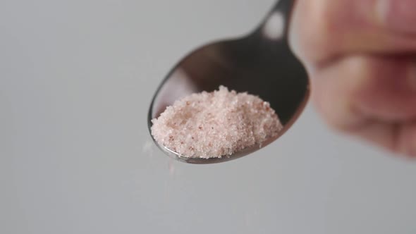 Full teaspoon of Himalayan pink salt in hand close-up. Falling seasoning crystals in slow motion
