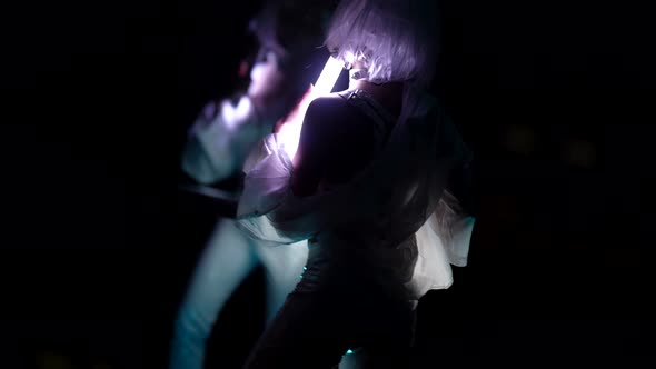 A Blonde in a White Suit Makes Dance Moves Standing Isolated Against a Dark Background in the Studio
