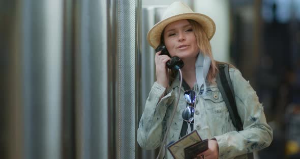 Happy Smiling Woman Calling From the Public Telephone To Friends at Airport