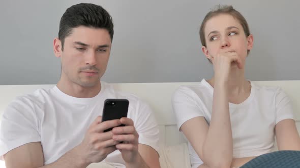 Man Using Smartphone Upset Girlfriend Sitting Aside