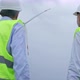 Engineers in white helmets with radio set and toolkit look at windmill generating. - VideoHive Item for Sale