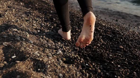 Barefoot Legs of Slim Young Woman Are Stepping Over Pebble Beach Near Seawater