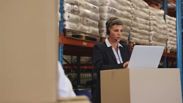 Female warehouse mananger in headset using laptop 4k