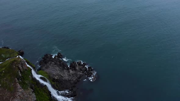 Overhead panning shot of a waterfall meeting the ocean in Iceland