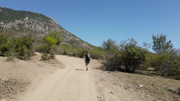 Girl Traveler Walks Alone in a Hat on the Road in the Mountains