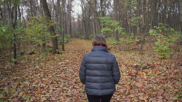 Senior Woman Goes on the Path Along the Autumnal Forest