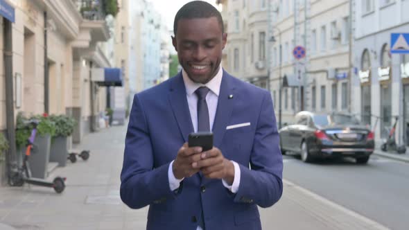 Walking African Businessman Browsing Internet on Smartphone