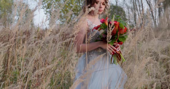 A Young Woman Dressed in a Gray Wedding Dress. She Has Flowers in Her Hand and Is in the Park