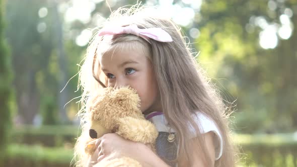 Pretty child girl playing with her favorite teddy bear toy outdoors in summer park.