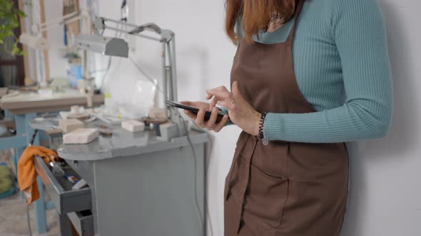 Crop View Of Young Artisan Browsing On Her Smartphone Inside Her Working Place