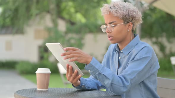 Young African Woman Reacting to Loss on Tablet in Outdoor Cafe