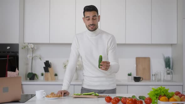 Portrait of Confident Male Middle Eastern Blogger Talking Holding Organic Healthful Cucumber in Hand