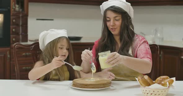 Caucasian Mother and Daughter Applying Condensed Milk on Baked Cake. Happy Family in Cook Hats and