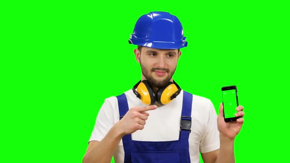 Man in a Builder's Suit Advertises a Smartphone. Green Screen. Mock Up