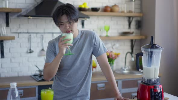 Young Happy Asian Man Smelling Tasty Milk Cocktail in Glass Smiling Looking at Camera