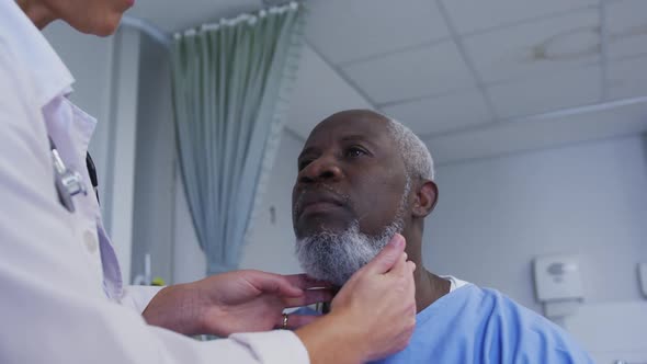 Caucasian female doctor examining neck of african american senior male patient at hospital