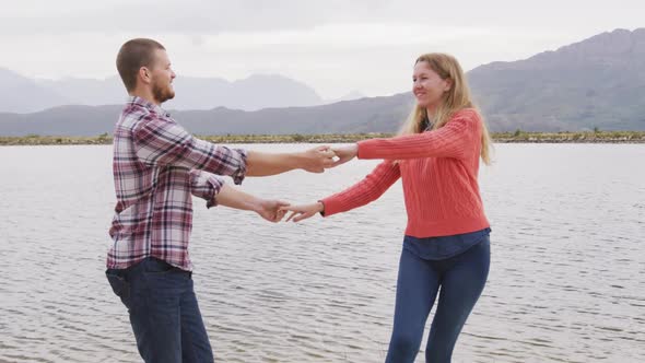 Caucasian couple having a good time on a trip to the mountains, dancing near lake and smiling