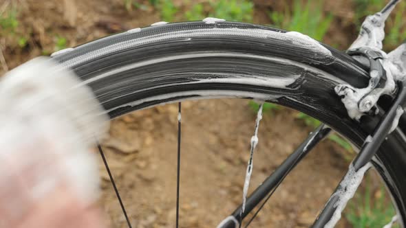 Bicycle washing. Man washes bike wheel with soap foam