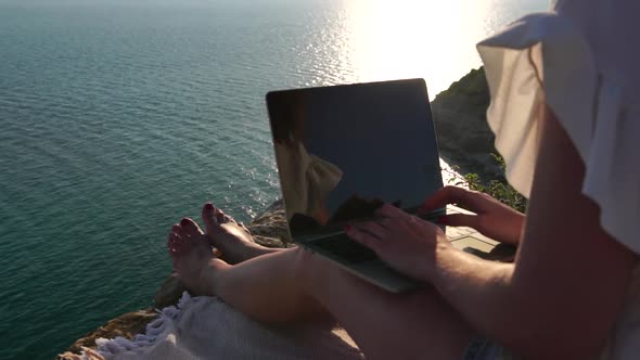 Successful Business Woman in Yellow Hat Working on Laptop By the Sea at Sunset Time