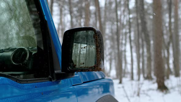 Dirty Blue Side View Mirror of SUV in Snowy Forest