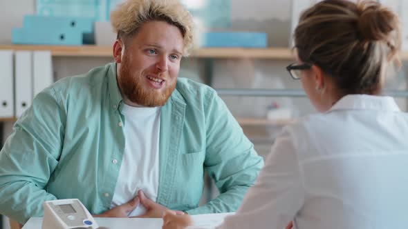 Overweight Man Complaining about Health to Doctor in Clinic